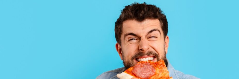 Homem sorridente comendo uma fatia de pizza, fundo da imagem em cor turquesa.